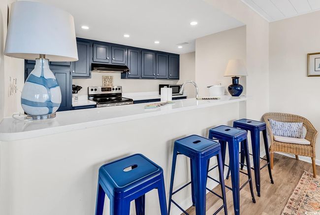 Kitchen featuring a peninsula, a breakfast bar, light countertops, electric stove, and light wood-style flooring | Image 12