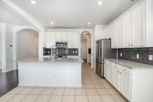 Kitchen with a sink, light tile patterned floors, stainless steel appliances, white cabinets, and arched walkways | Image 10
