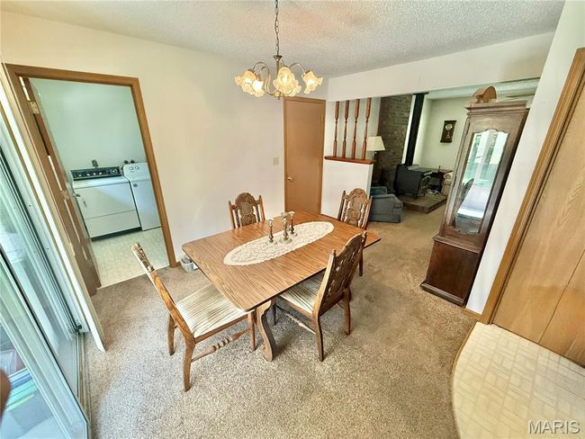 Carpeted dining space featuring washing machine and clothes dryer, a wood stove, a chandelier, and a textured ceiling | Image 21