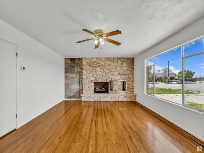 Unfurnished living room featuring a stone fireplace, ceiling fan, wood finished floors, and visible vents | Image 5