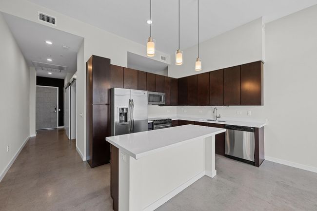 Kitchen featuring concrete flooring, dark brown cabinets, appliances with stainless steel finishes, a sink, and visible vents | Image 6