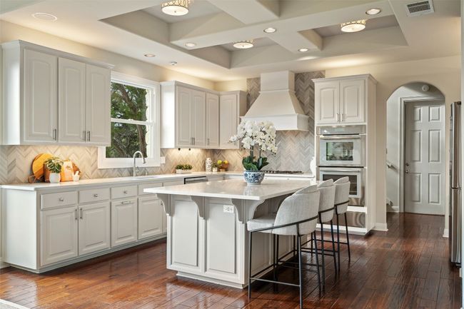 Kitchen with custom exhaust hood, coffered ceiling, a kitchen breakfast bar, dark wood-type flooring, and white cabinetry | Image 16