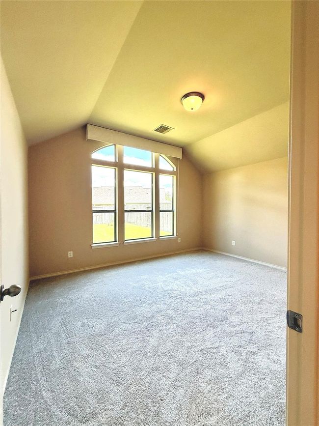 This is a bright, spacious bedroom with a high ceiling, featuring a large arched window that lets in plenty of natural light. It has neutral walls and fresh carpeting, creating a warm and inviting atmosphere. | Image 13
