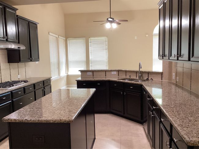 Kitchen with stovetop, a sink, a ceiling fan, range hood, and backsplash | Image 8