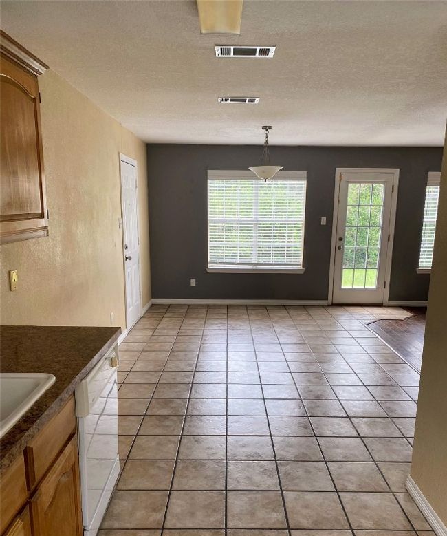 Unfurnished dining area featuring visible vents, baseboards, a textured ceiling, and light tile patterned floors | Image 9