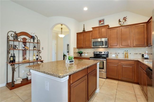 Kitchen featuring appliances with stainless steel finishes, light stone counters, backsplash, light tile patterned floors, and a kitchen island | Image 7