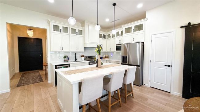 Kitchen featuring stainless steel appliances, light wood finished floors, light countertops, wine cooler, and backsplash | Image 11