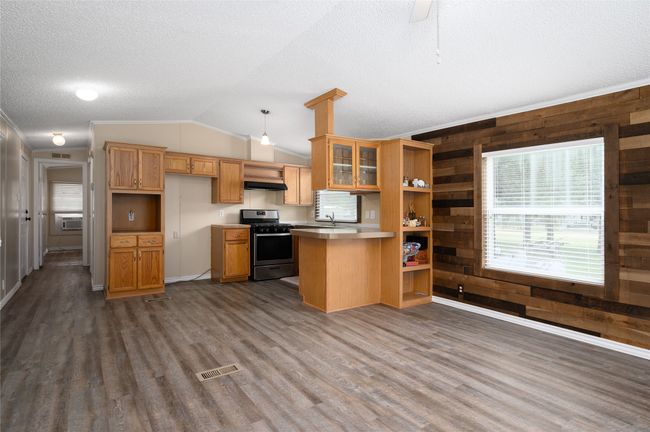 Kitchen with stainless steel gas range oven, dark wood-style floors, a peninsula, lofted ceiling, and wood walls | Image 23