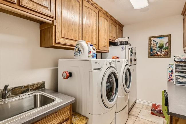 Laundry area with a sink, cabinet space, light tile patterned floors, baseboards, and washing machine and clothes dryer | Image 27