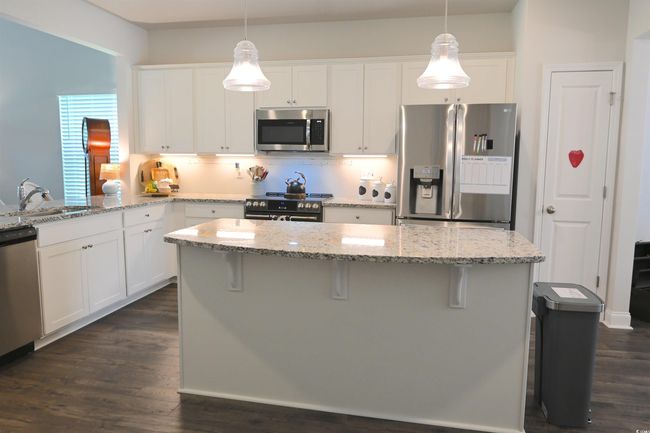 Kitchen featuring stainless steel appliances, white cabinets, a kitchen breakfast bar, dark wood-style floors, and light stone countertops | Image 5