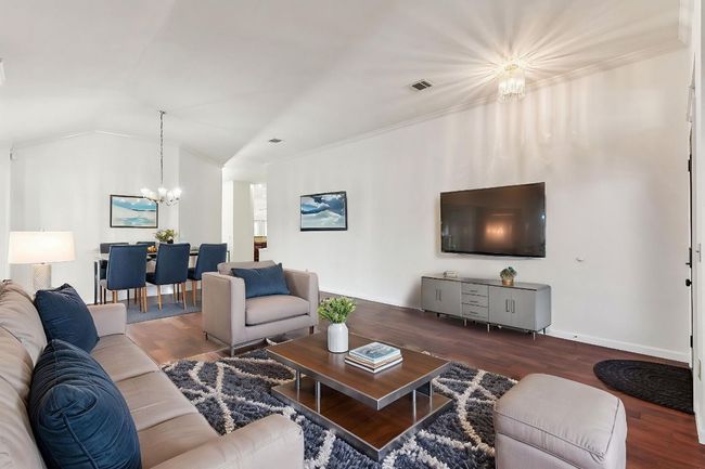 Living area featuring a chandelier, lofted ceiling, wood finished floors, crown molding, and baseboards | Image 6