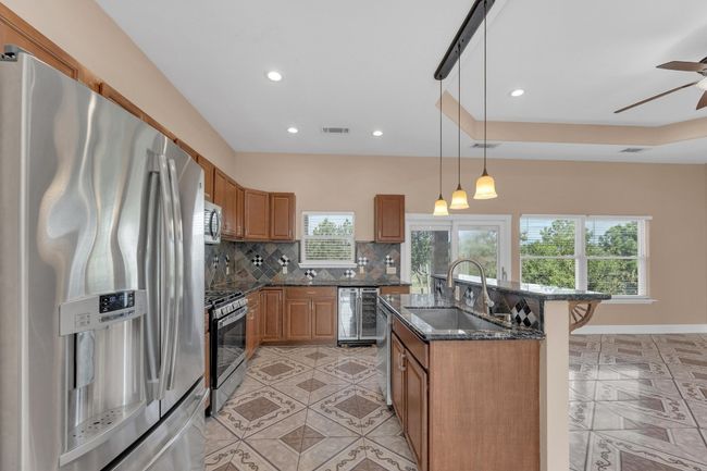 Kitchen with appliances with stainless steel finishes, backsplash, wine cooler, an island with sink, and a ceiling fan | Image 16