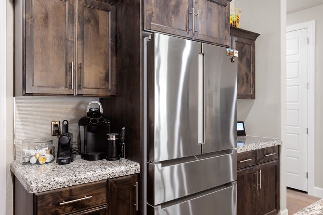 Kitchen featuring freestanding refrigerator, dark brown cabinetry, backsplash, light stone counters, and light wood-style floors | Image 44