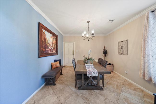 This dining room features a cozy, inviting space with tile flooring. The walls are painted in a soothing blue and beige, adorned with a modern chandelier, enhancing the room's warm ambiance. | Image 6
