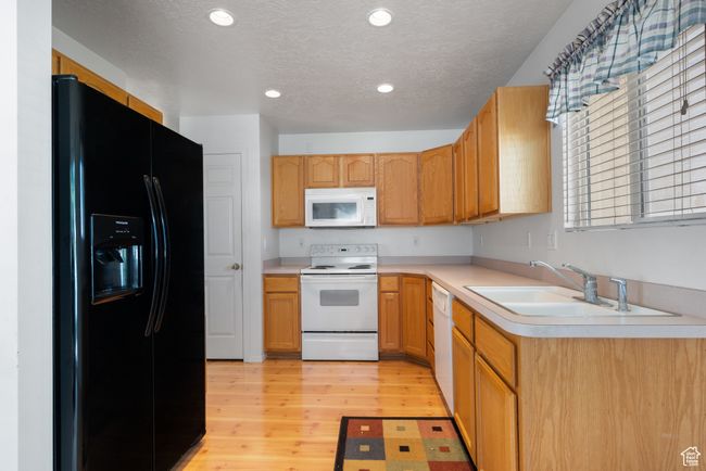 Kitchen with white appliances, light countertops, light wood-style flooring, a textured ceiling, and recessed lighting | Image 9