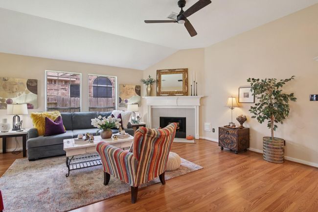 This inviting living room features a high ceiling with a ceiling fan, a cozy fireplace, and large windows that fill the space with natural light. | Image 6