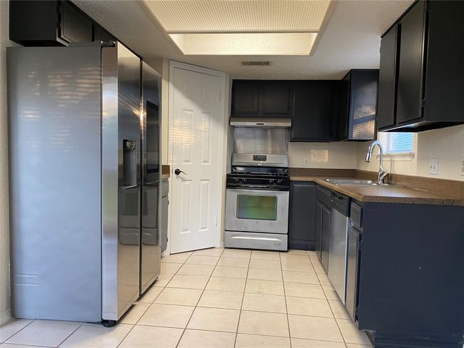 Kitchen with light tile patterned floors, dark countertops, under cabinet range hood, appliances with stainless steel finishes, and a sink | Image 15