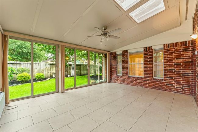 Surrounded by walls of glass, this light-filled sunroom offers beautiful backyard views and year-round enjoyment. With tile flooring, skylights, 2 sliding doors, a doggie door. and a ceiling fan, it's the perfect spot to relax, entertain, or create a flexible second living space. This fully enclosed space is both air conditioned and heated for year-round comfort. | Image 34