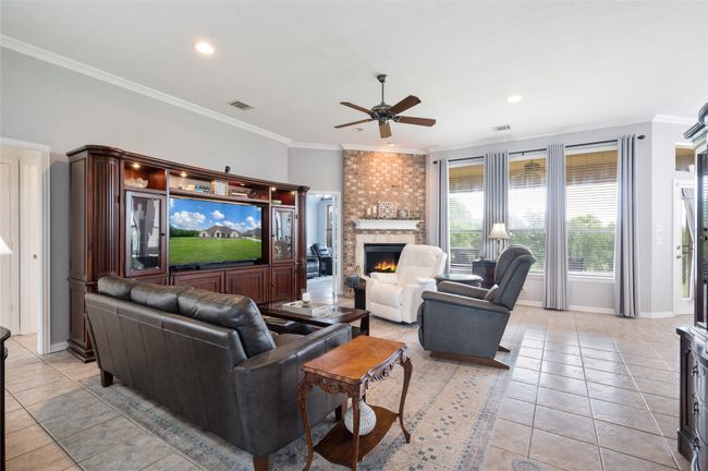 Living room with a ceiling fan, light tile patterned floors, a brick fireplace, crown molding, and recessed lighting | Image 5
