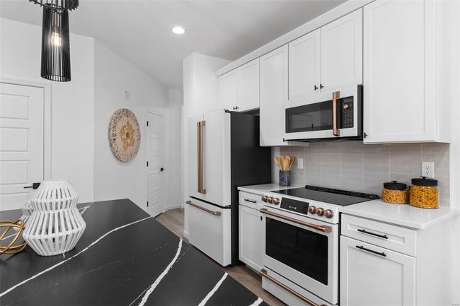 Kitchen with decorative backsplash, white cabinetry, hardwood / wood-style floors, and high quality appliances | Image 6