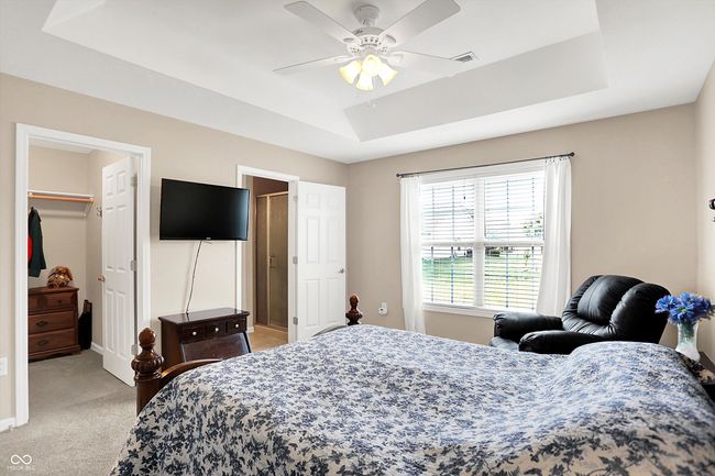bedroom featuring a raised ceiling, light carpet, a spacious closet, a closet, and ceiling fan | Image 23