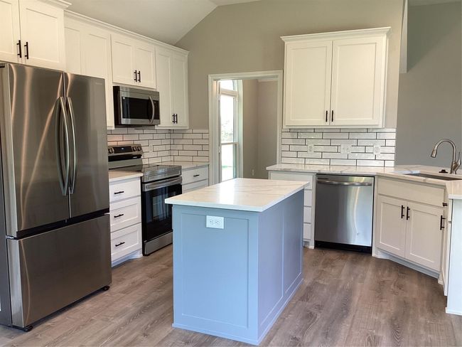 Kitchen featuring appliances with stainless steel finishes, vaulted ceiling, backsplash, and wood finished floors | Image 10
