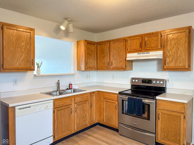 kitchen featuring electric range, under cabinet range hood, light countertops, a sink, and white dishwasher | Image 9