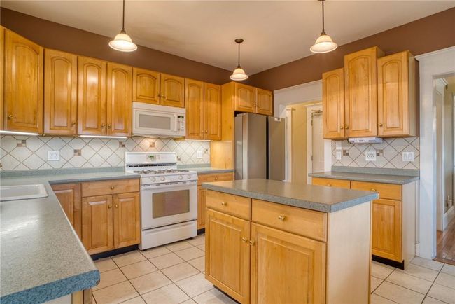 Kitchen with light tile patterned floors, decorative backsplash, a kitchen island, and white appliances | Image 8