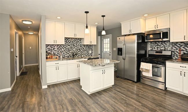 Kitchen with pendant lighting, a center island, dark hardwood / wood-style flooring, white cabinetry, and stainless steel appliances | Image 5