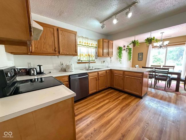 kitchen with stainless steel dishwasher, black range with electric cooktop, a peninsula, light wood finished floors, and light countertops | Image 21