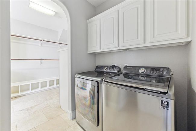 Bright laundry room featuring stainless steel washer and dryer units, with white cabinets above for storage and an open walk-in closet area adjacent for organization. | Image 21