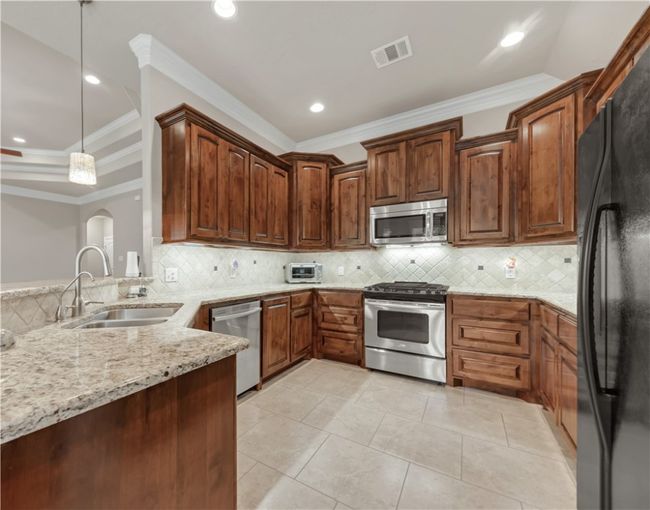 Kitchen featuring appliances with stainless steel finishes, a sink, crown molding, light stone countertops, and tasteful backsplash | Image 12