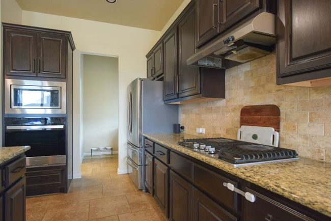 Kitchen with dark brown cabinetry, under cabinet range hood, decorative backsplash, and stainless steel appliances | Image 4