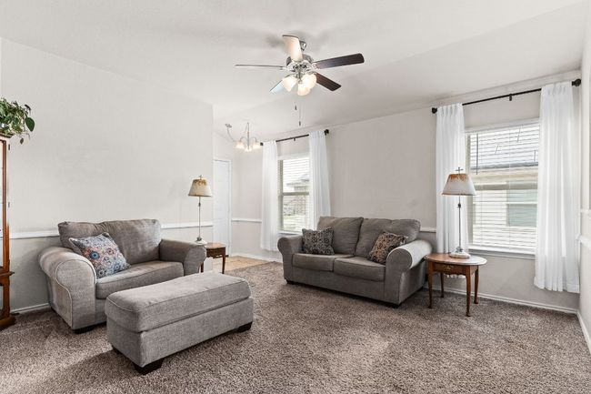 Carpeted living area with baseboards and ceiling fan with notable chandelier | Image 6