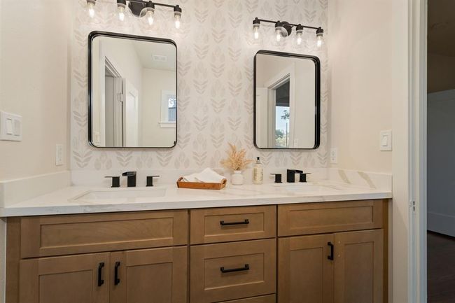 The shared Hollywood bathroom features dual sinks accented by matte black framed mirrors and chic farmhouse-style vanity light fixtures. Ample storage is provided by spacious under-cabinetry and centered drawers. | Image 27