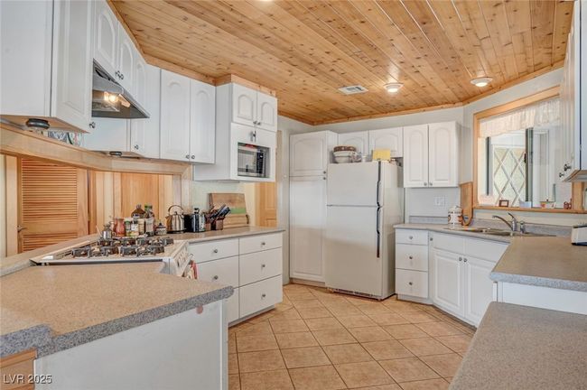 Kitchen with white appliances, under cabinet range hood, a sink, light tile patterned floors, and wooden ceiling | Image 29