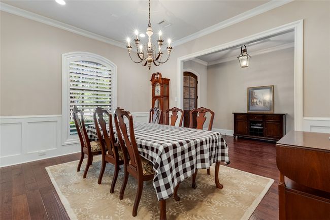 Dining area with a chandelier, arched walkways, dark wood finished floors, wainscoting, and crown molding | Image 5