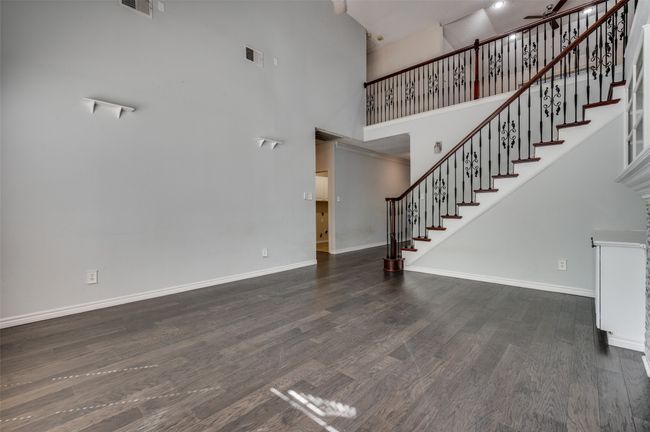 Unfurnished living room featuring visible vents, baseboards, wood finished floors, and a high ceiling | Image 8