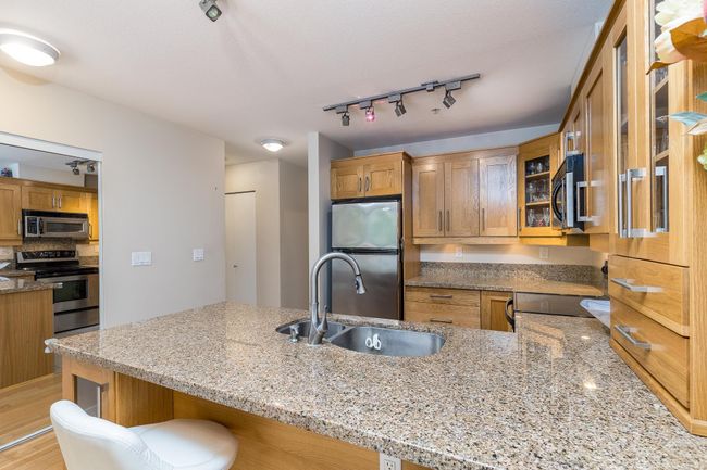 Kitchen with stainless steel appliances, a peninsula, a sink, light stone counters, and track lighting | Image 5
