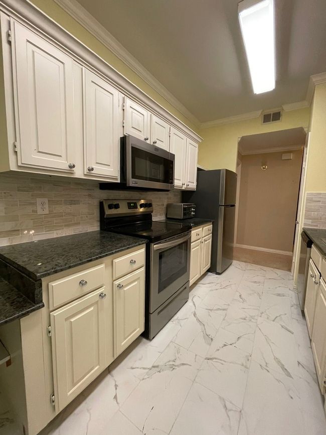 Kitchen with stove, ornamental molding, refrigerator, light marble finish flooring, and tasteful backsplash | Image 7