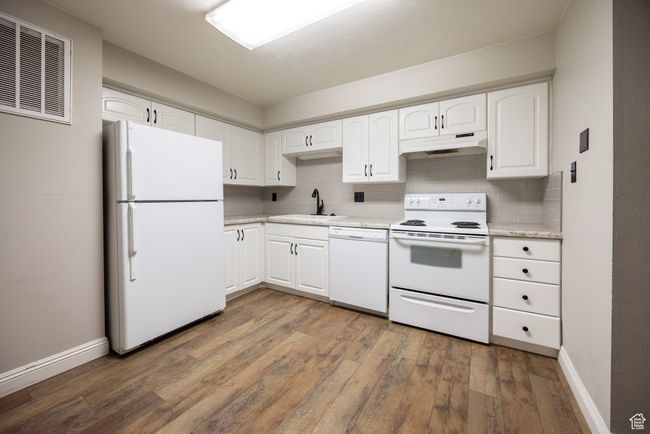 Kitchen with white appliances, under cabinet range hood, hardwood / wood-style flooring, decorative backsplash, and white cabinets | Image 4