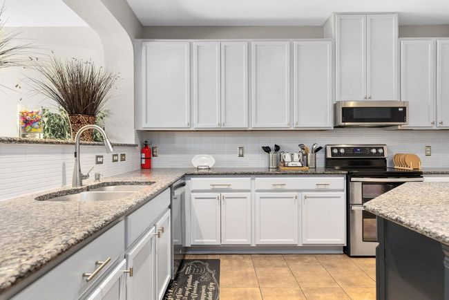Kitchen featuring stainless steel appliances, a sink, backsplash, and light stone countertops | Image 9