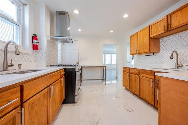Kitchen featuring stainless steel gas range oven, tasteful backsplash, a sink, and island exhaust hood | Image 8