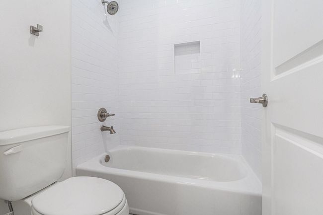 This bathroom features a clean, modern design with white subway tiles, a built-in shower niche, and brushed nickel fixtures. It includes a classic bathtub and a toilet, offering a fresh and simple aesthetic. | Image 37