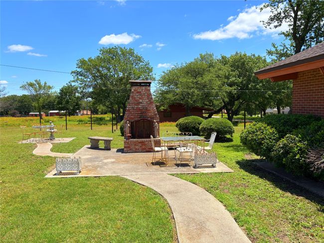 View of grassy yard featuring an outdoor brick fireplace and a patio area | Image 15