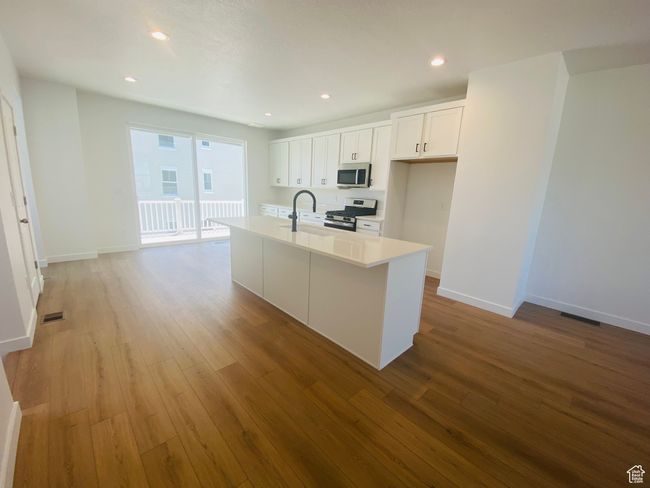Kitchen featuring stainless steel appliances, light wood-style flooring, white cabinets, light countertops, and recessed lighting | Image 9