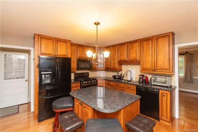 Kitchen featuring light wood-type flooring, pendant lighting, black appliances, an inviting chandelier, and a center island | Image 3