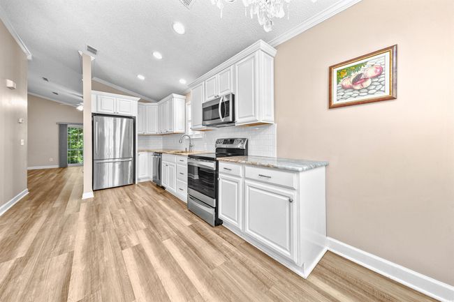 Kitchen featuring white cabinets, light wood-style floors, stainless steel appliances, tasteful backsplash, and vaulted ceiling | Image 25