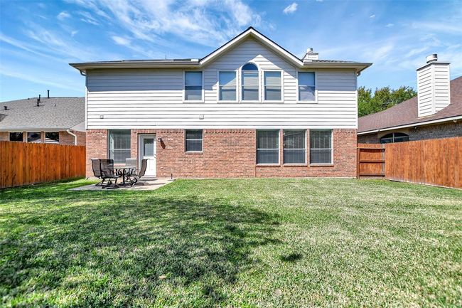 This home features a spacious backyard with a well-maintained lawn, bordered by a wooden fence for privacy. The exterior showcases a combination of brick and siding, with large windows allowing ample natural light. A small patio area provides space for outdoor seating and relaxation. | Image 45
