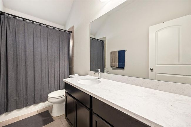 Secondary bath features tile flooring, bath/shower combo with tile surround, dark wood cabinets, beautiful light countertops, mirror, dark, sleek fixtures and modern finishes. | Image 18